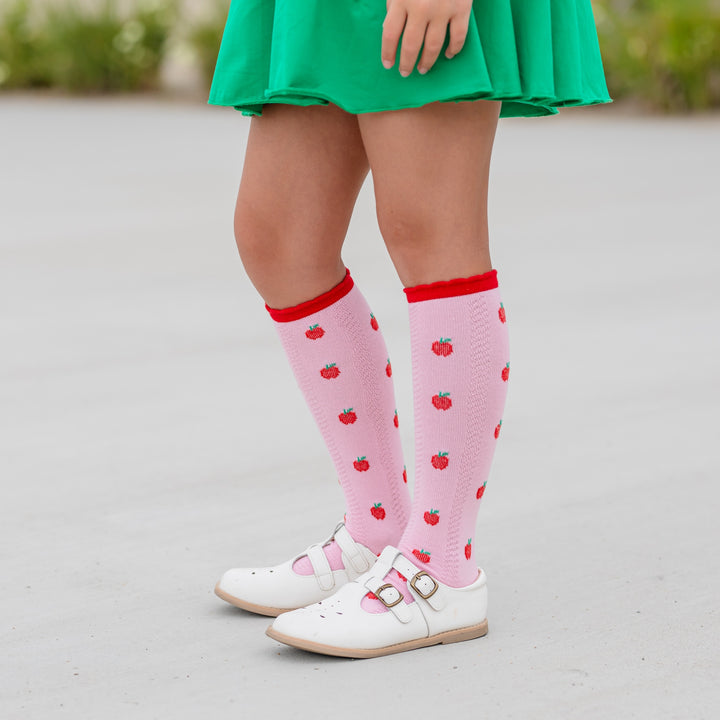 girl wearing pink knee high socks with red apples and red scallop trim with matching green skort