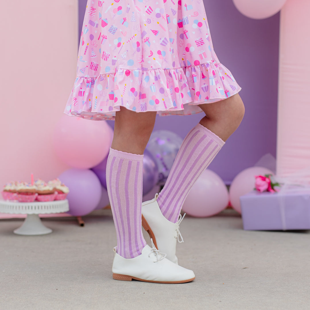girl in pink birthday twirl dress and matching purple striped knee high socks