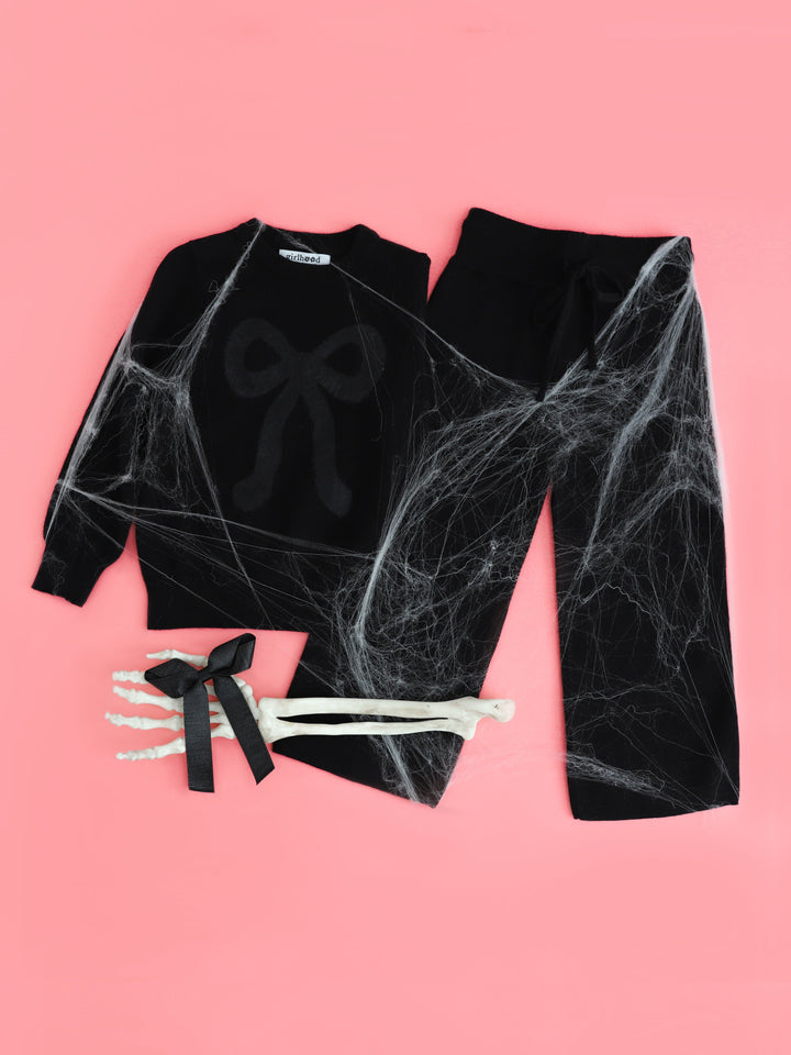 flatlay photo styled with webs and skelly hand for girls' black pullover cotton knit sweater with black fluffy bow design, black knit sweater pants and shimmery black ribbon bow