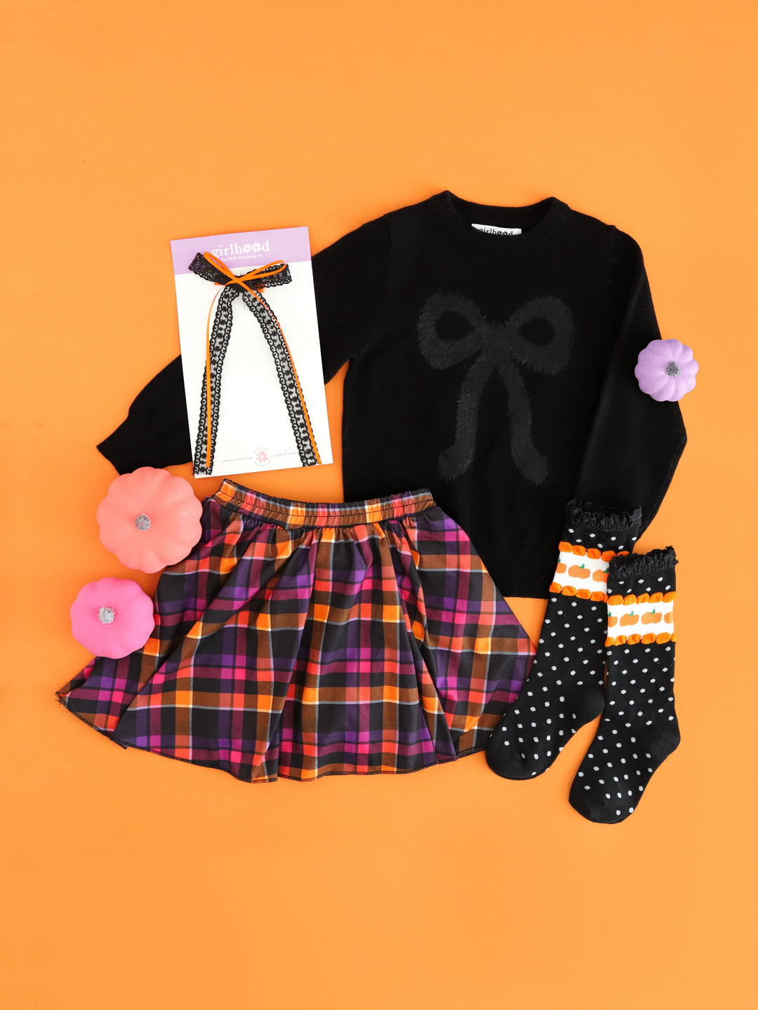 girls' Halloween outfit inspo featuring black knit sweater with fluffy black bow design, Halloween plaid skort, pumpkin dot knee highs and matching lace bow