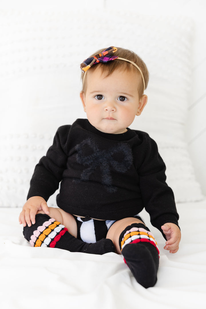 baby girl in black knit sweater set with black fluffy bow design, plaid velvet baby bow headband and matching striped bubble socks for Halloween