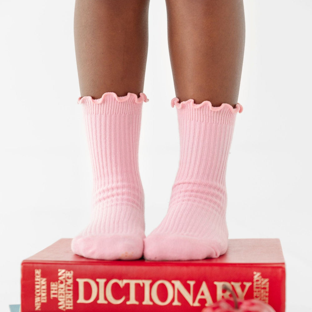 little girl standing on school books wearing light pink ribbed lettuce trim midi socks
