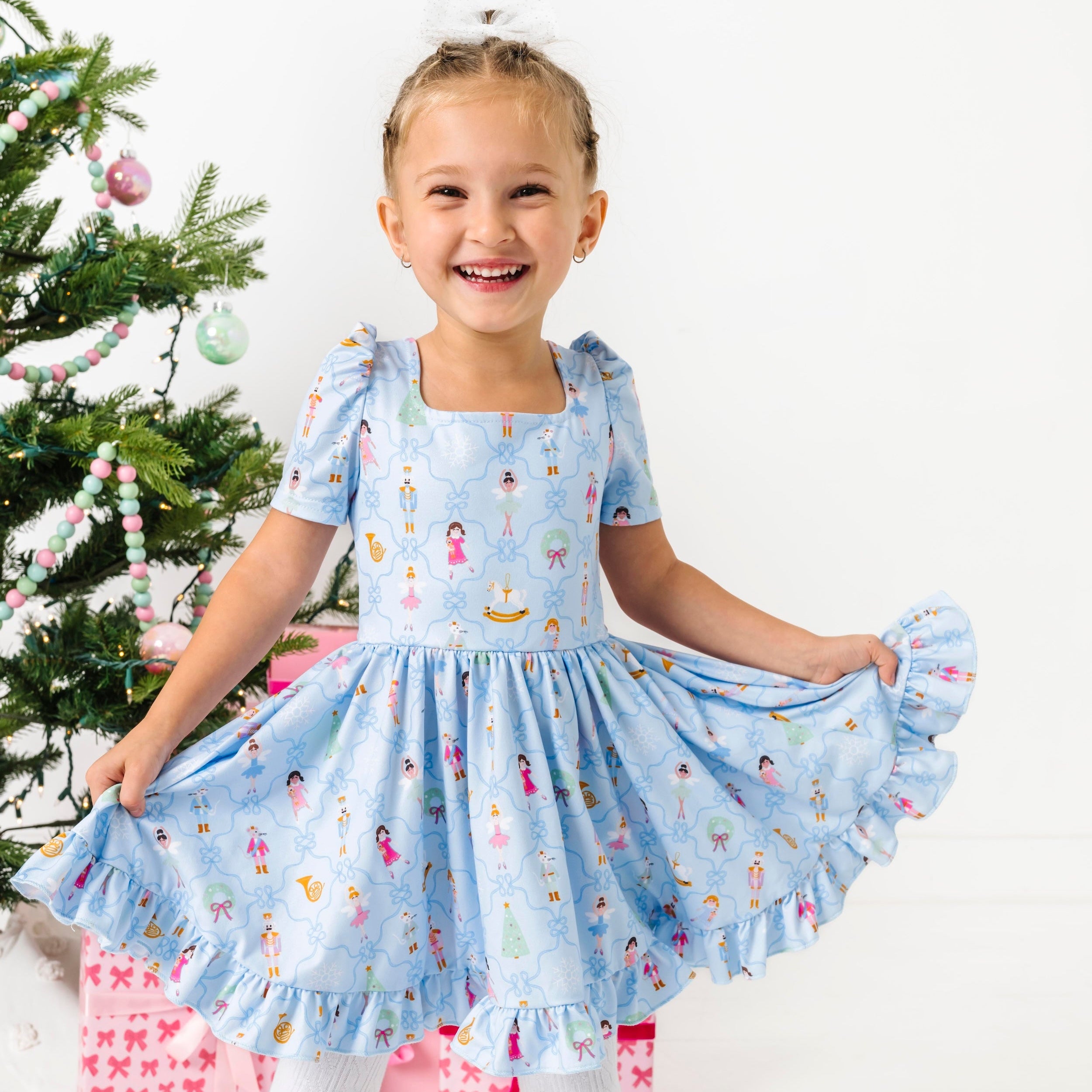 little girl twirling in blue nutcracker christmas dress in front of Christmas tree