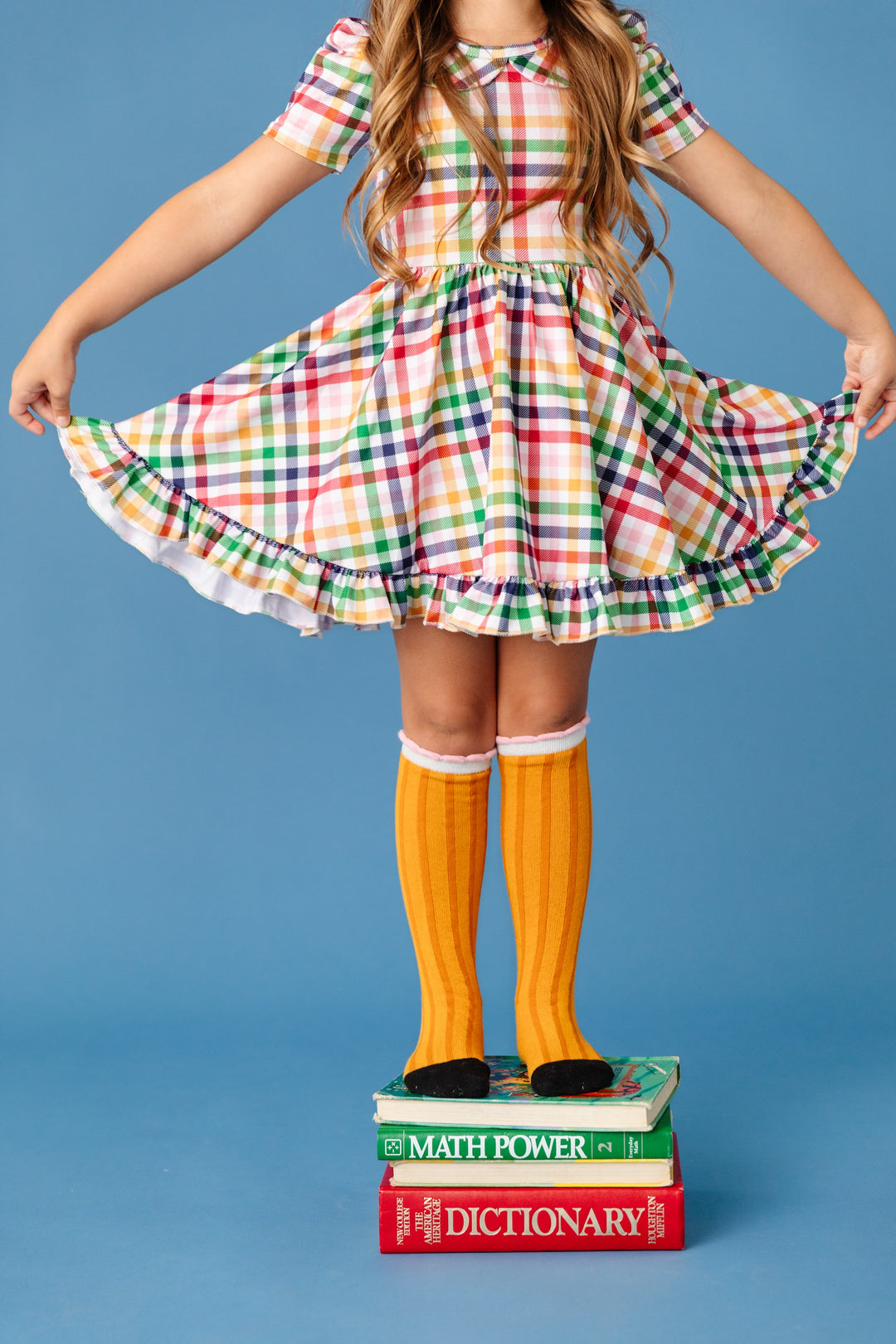 girl holding out rainbow gingham plaid twirl dress with pencil knee high socks for back to school