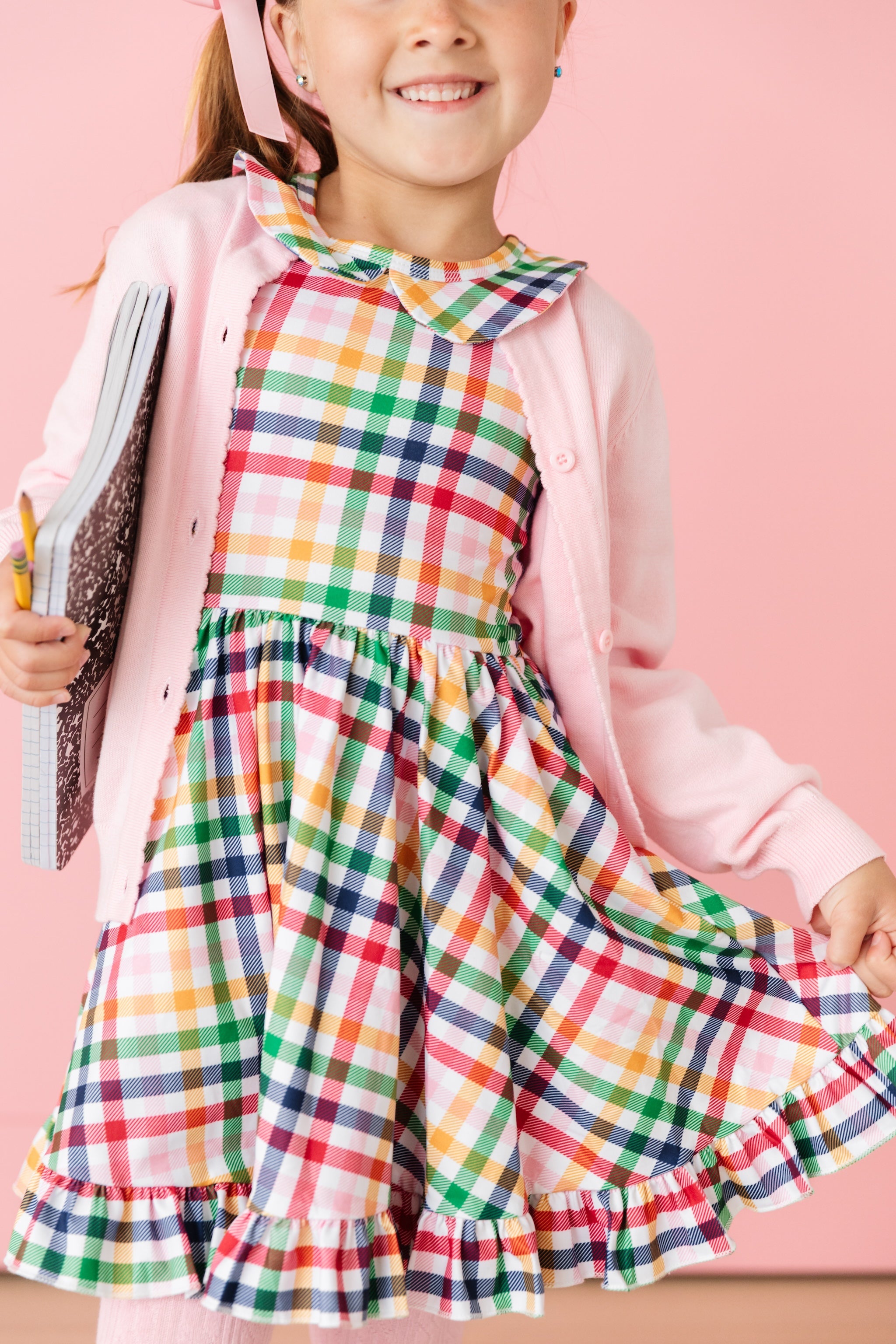girl in short sleeve collared twirl dress in primary rainbow plaid print for back to school with matching pink cardigan