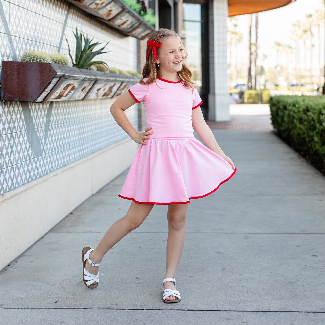 girl sandals wearing matching two-tone summer separates featuring pink fitted top and skort with red binding and a matching red satin ribbon bow.