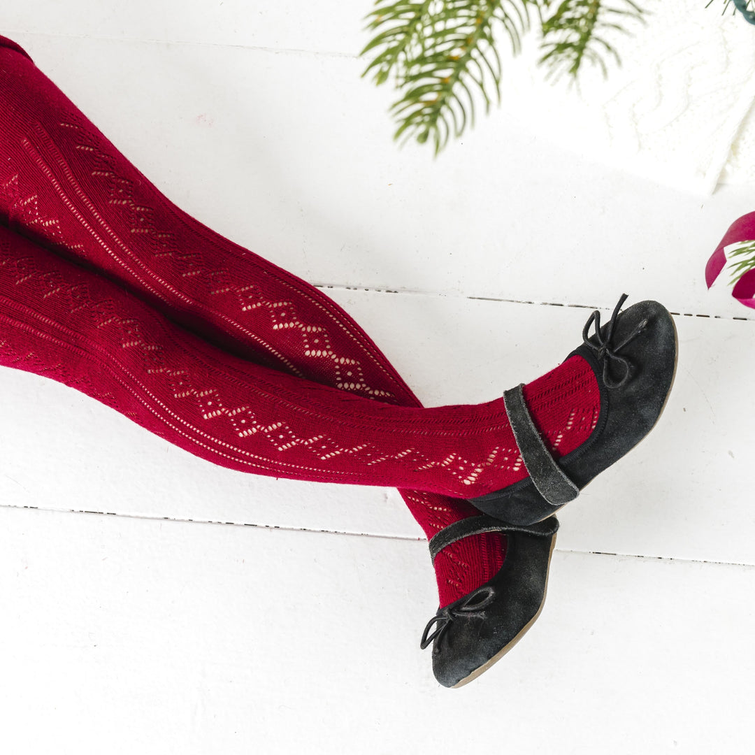 closeup of girl by Christmas tree in open knit crimson red tights and black mary janes