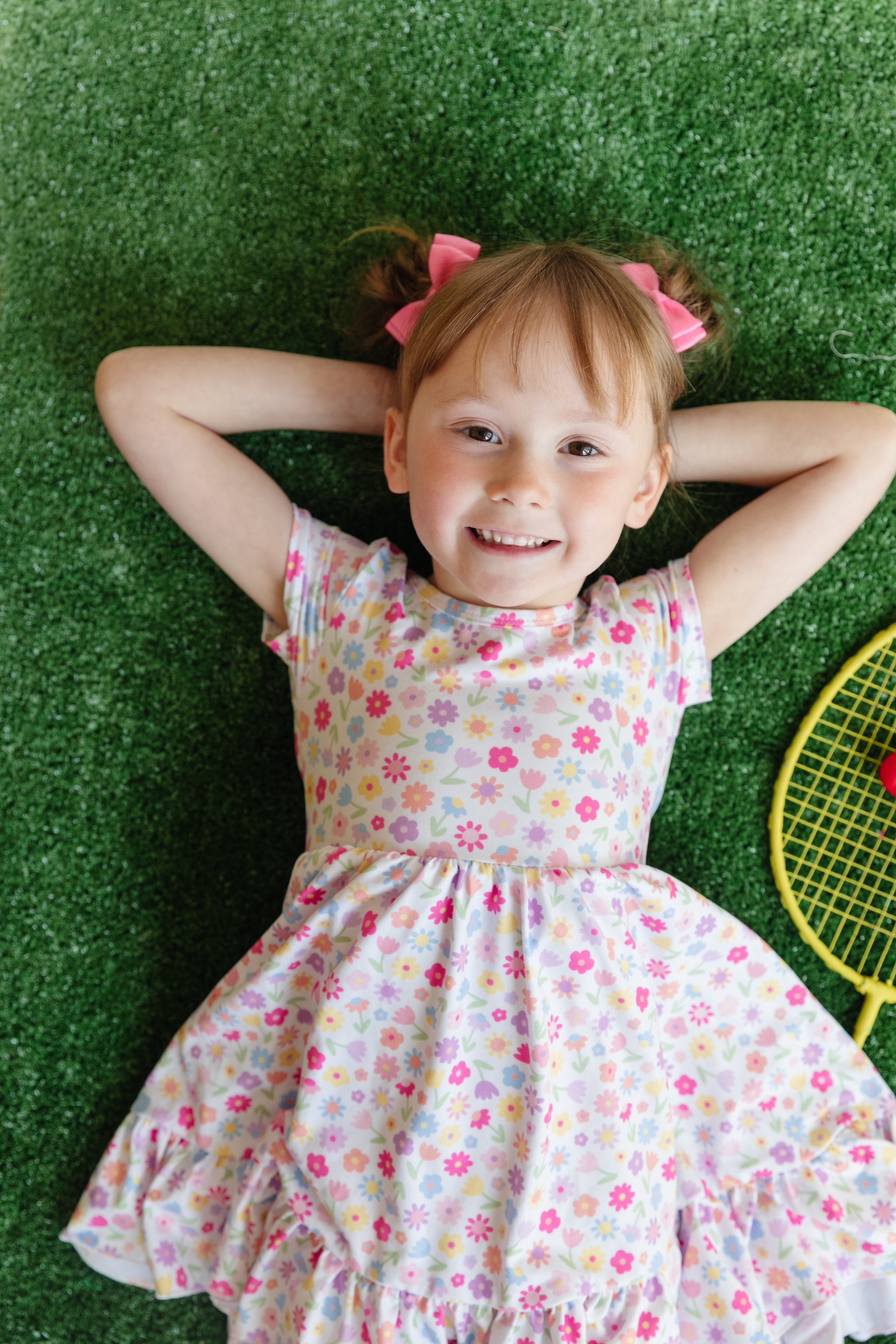 little girl laying on grass in pastel floral print on white twirl dress for spring and summer