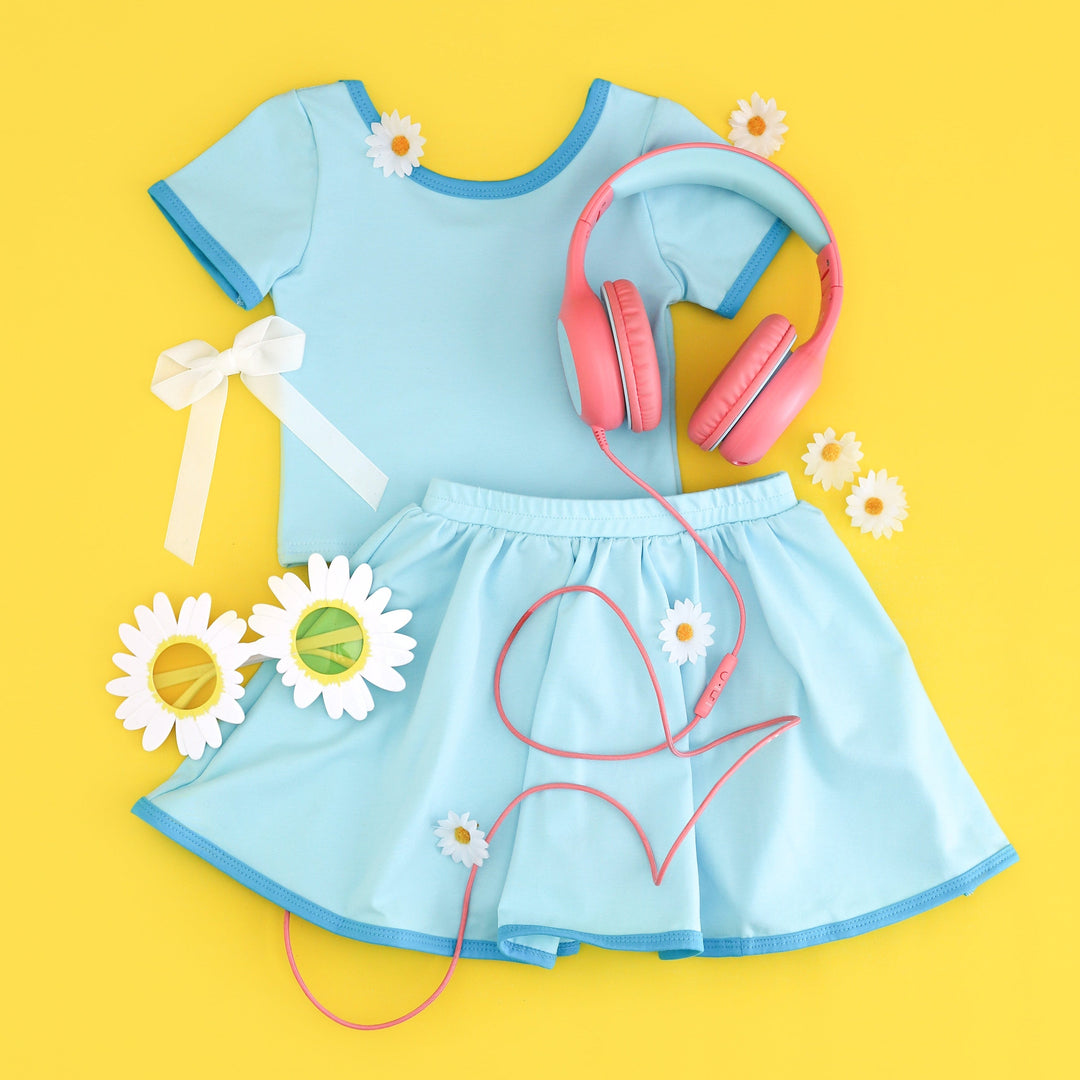 Girls's bright blue top and matching skort with pink headphones and decorative items on a yellow background