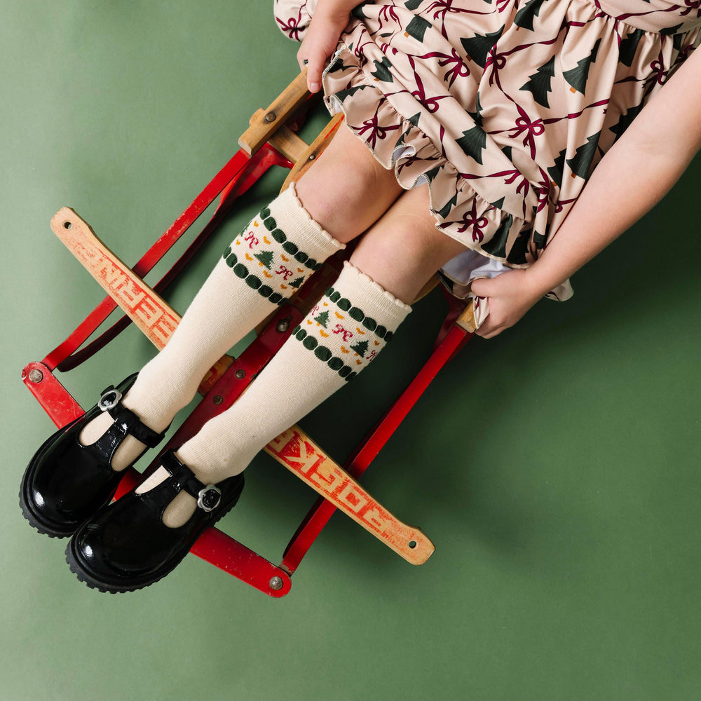 little girl on sled with cream scalloped knee-high socks with faire-isle design at the calf and matching Christmas tree dress