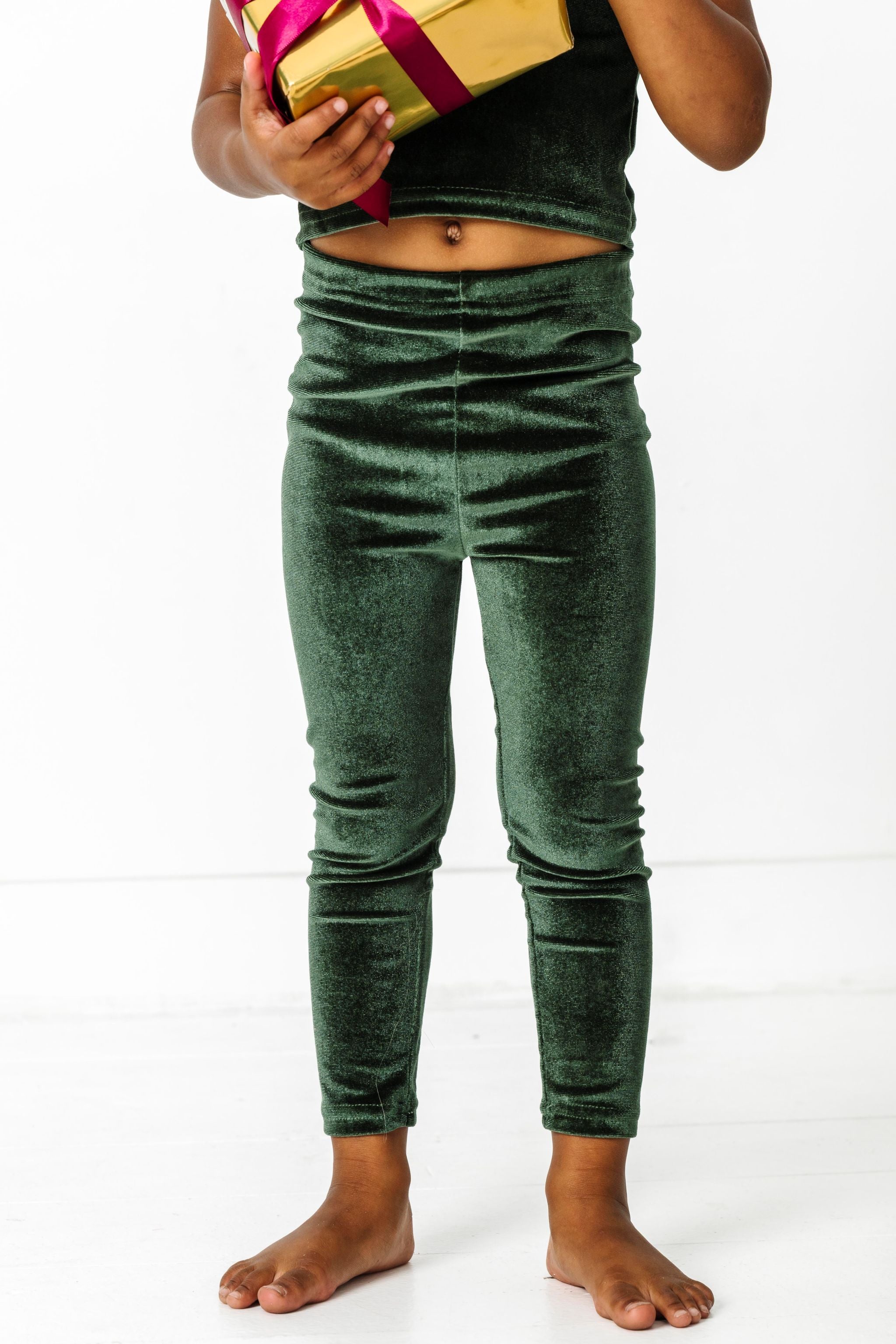 little girl holding Christmas gift in forest green velvet leggings and matching top