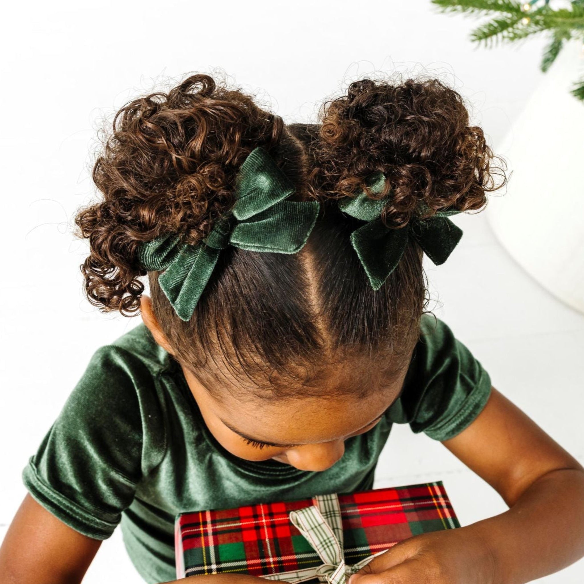 little girl holding Christmas gifts in forest green velvet outfit with matching pigtail bows on clips