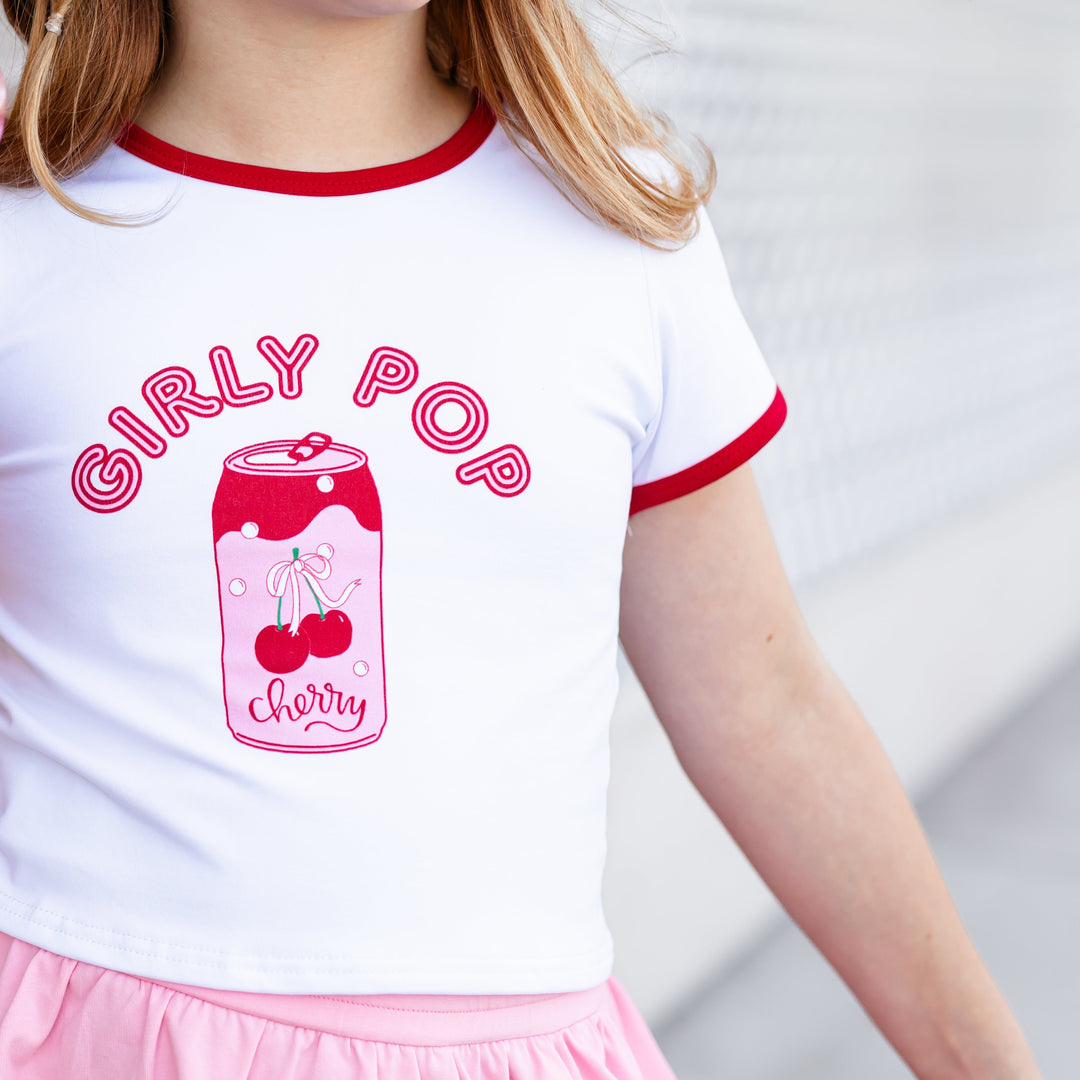 closeup of pink and red girly pop print and cherry soda design on little girl's white tee