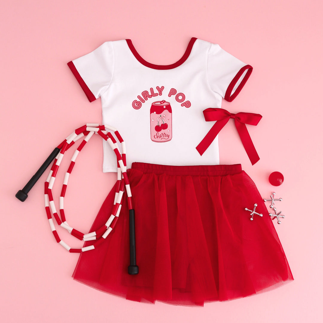 styled summer flatlay photo featuring "girly pop" tee and red tutu skirt with built in biker shorts and matching red bow