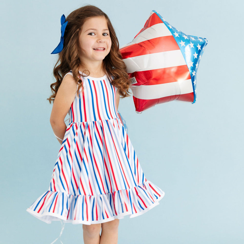 little girl in 4th of july striped tank top dress holding star shaped american flag balloon