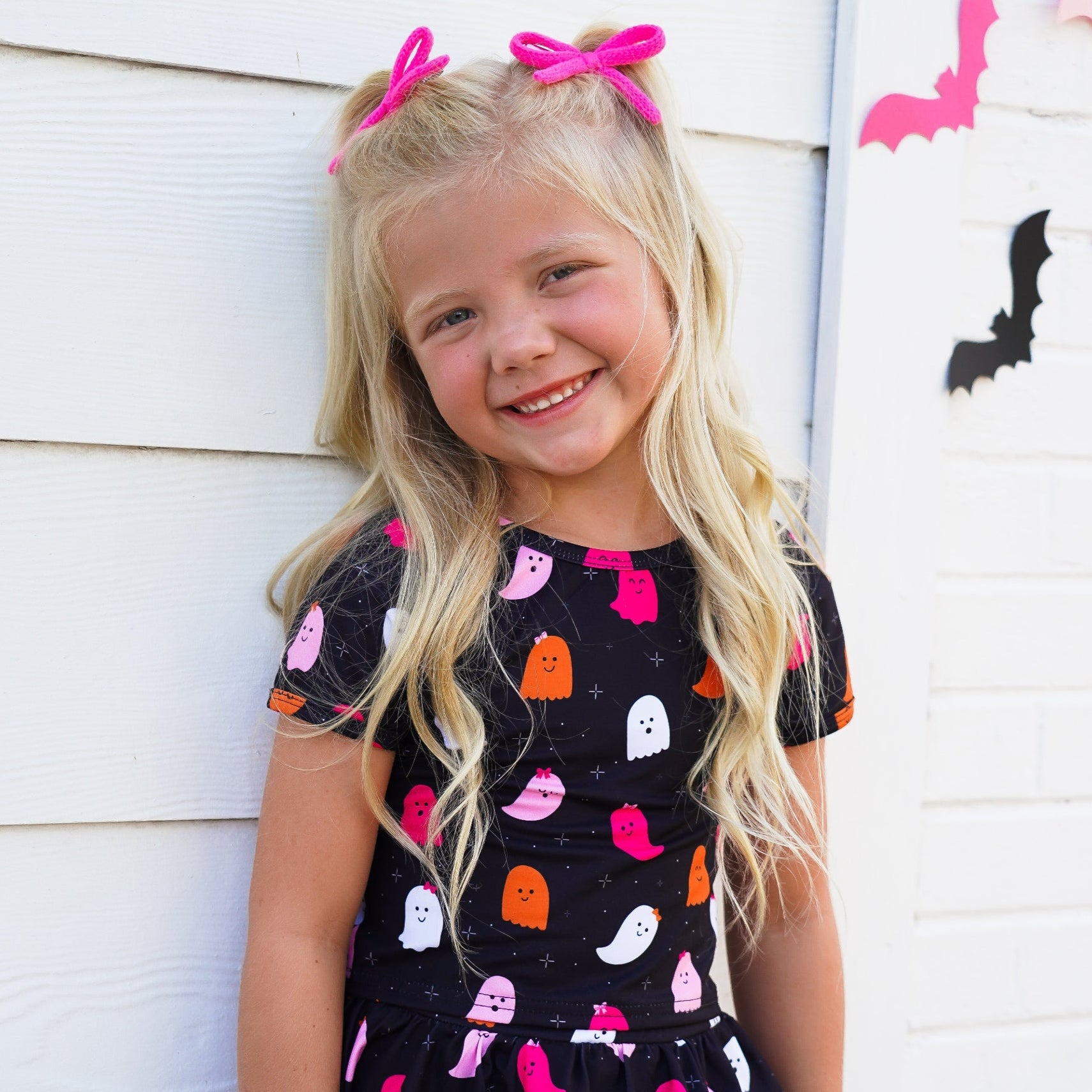 little girl in matching black with colorful ghost print top and skort paired with pink yarn pigtail bows