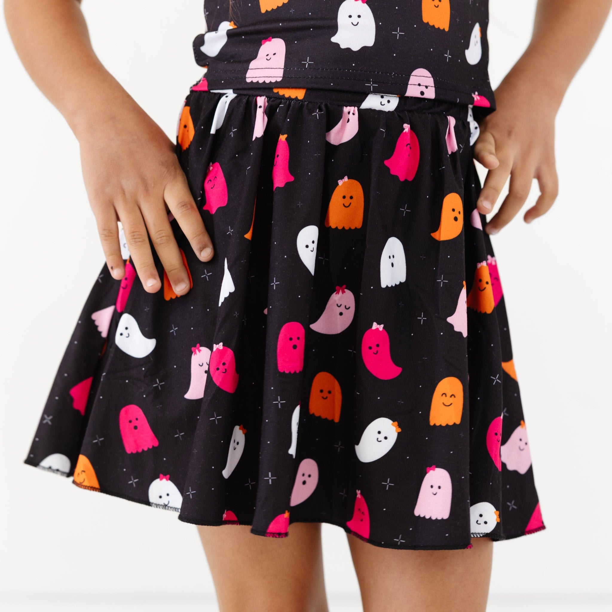 little girl in printed black skort with ghosts wearing little bows and matching top for Halloween