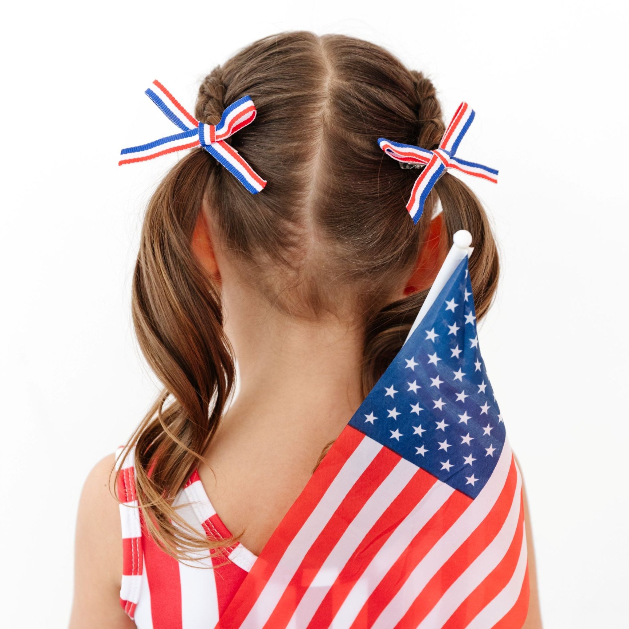 little girl in red, white and blue striped pigtail bows holding flag in American Flag inspired tutu dress