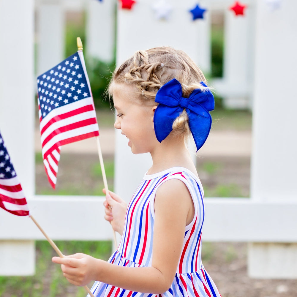little girl wearing striped 4th of july dress with bright blue linen hair bow in her hair