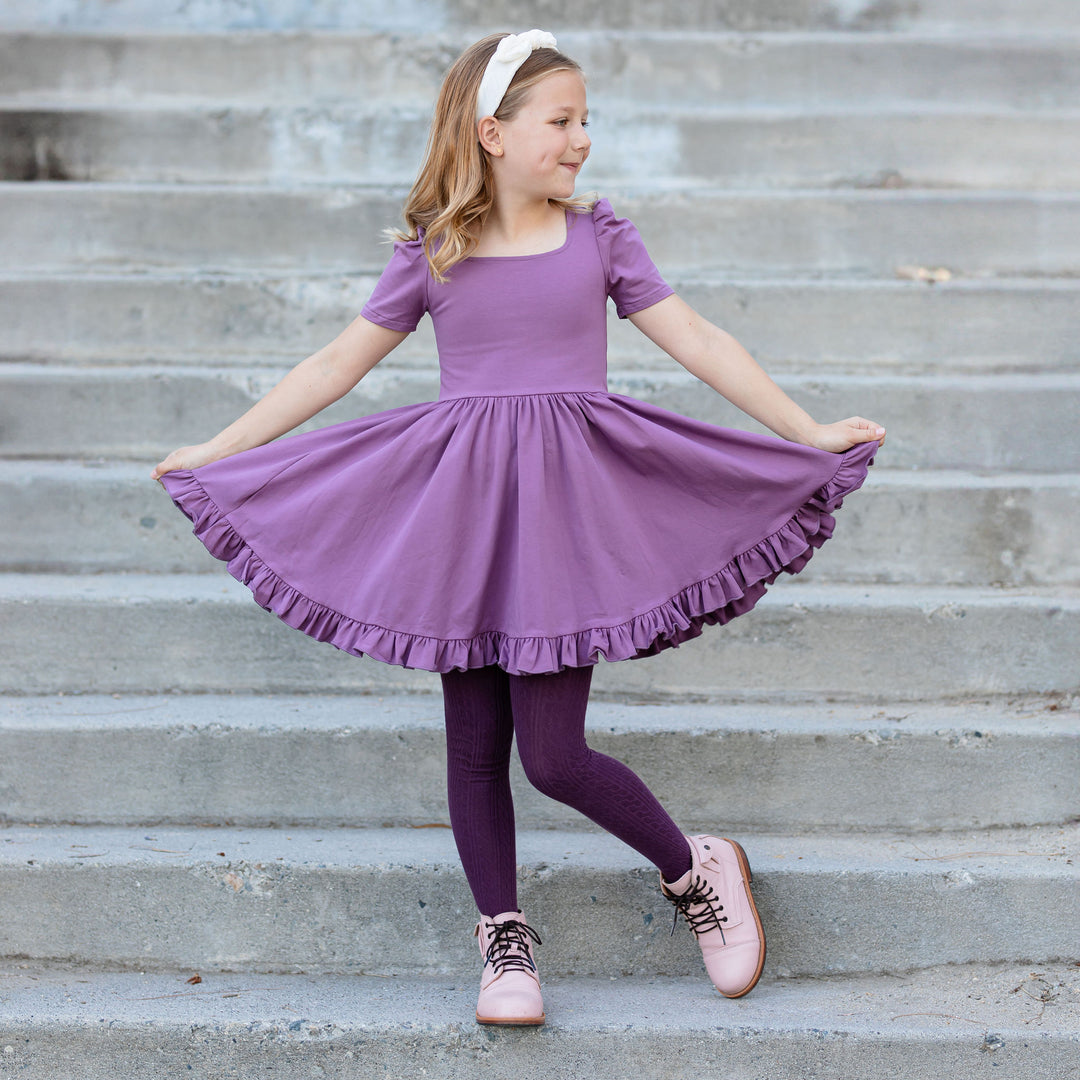 little girl wearing twirly purple cotton dress with coordinating dark purple cable knit tights
