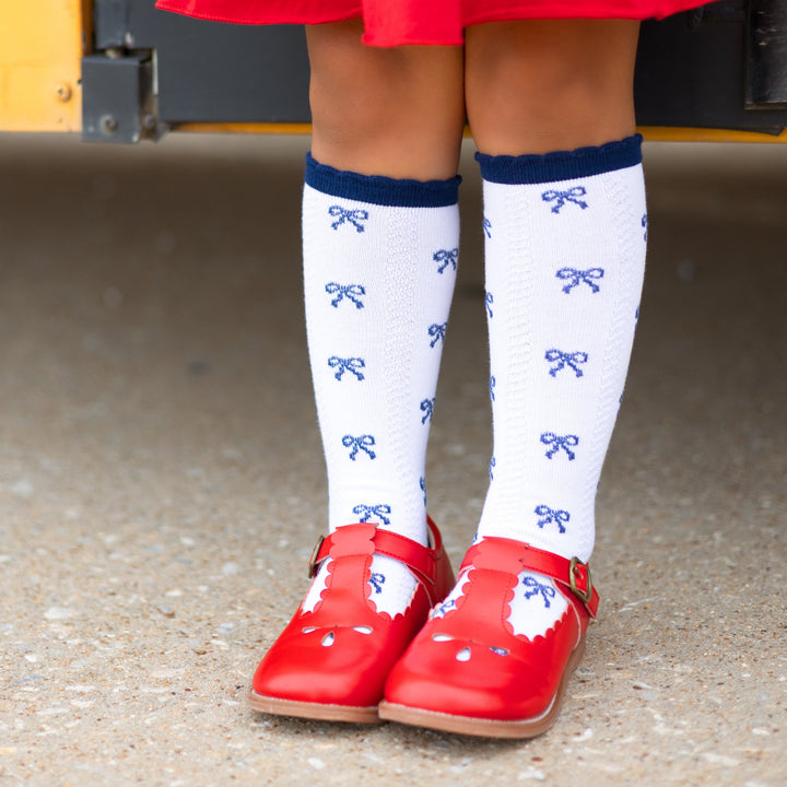 girl in white knee high socks with navy bows on them and navy scallop trim and red shoes