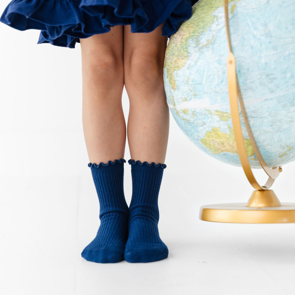 little girl holding globe in navy blue lettuce trin midi socks and matching navy blue uniform twirl dress