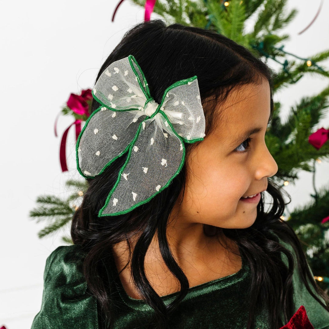 Young girl wearing a large decorative headband in front of a Christmas tree.
