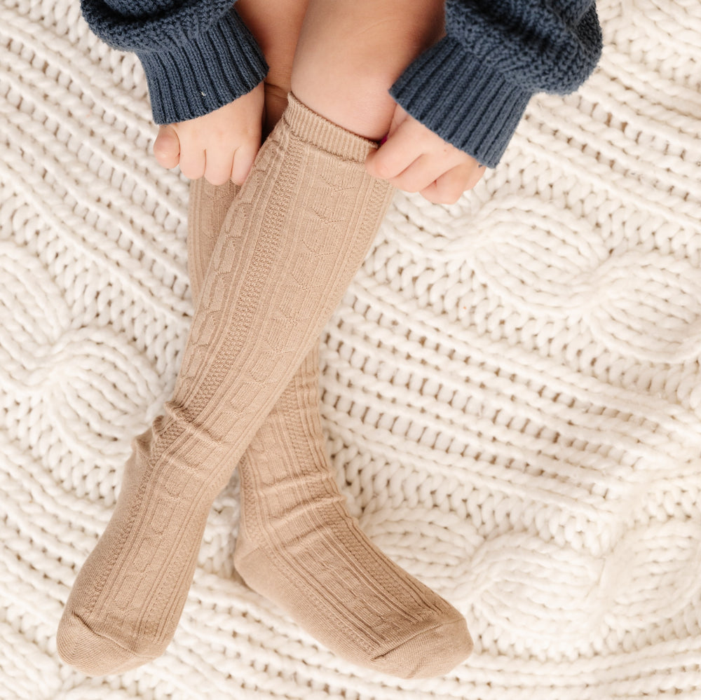 girl pulling up oat brown cable knit socks