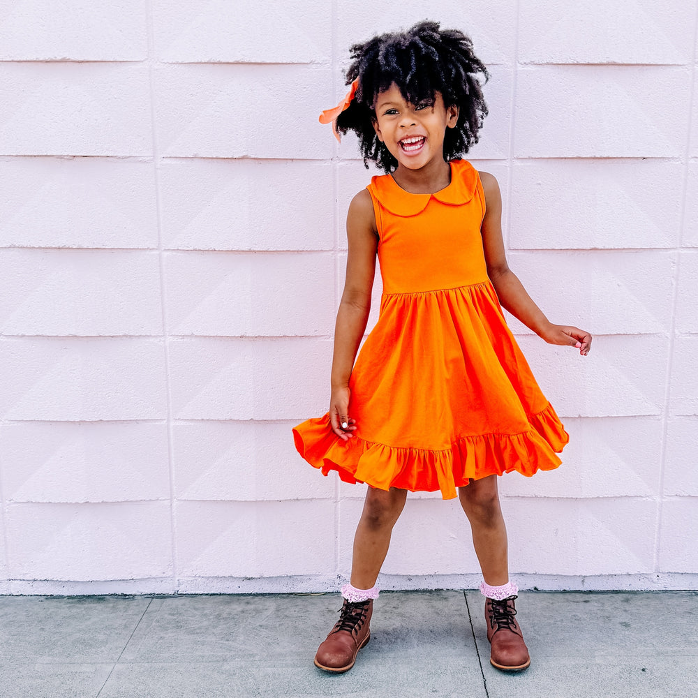 little girl wearing bright orange summer tank dress with lace trimmed socks and brown leather boots