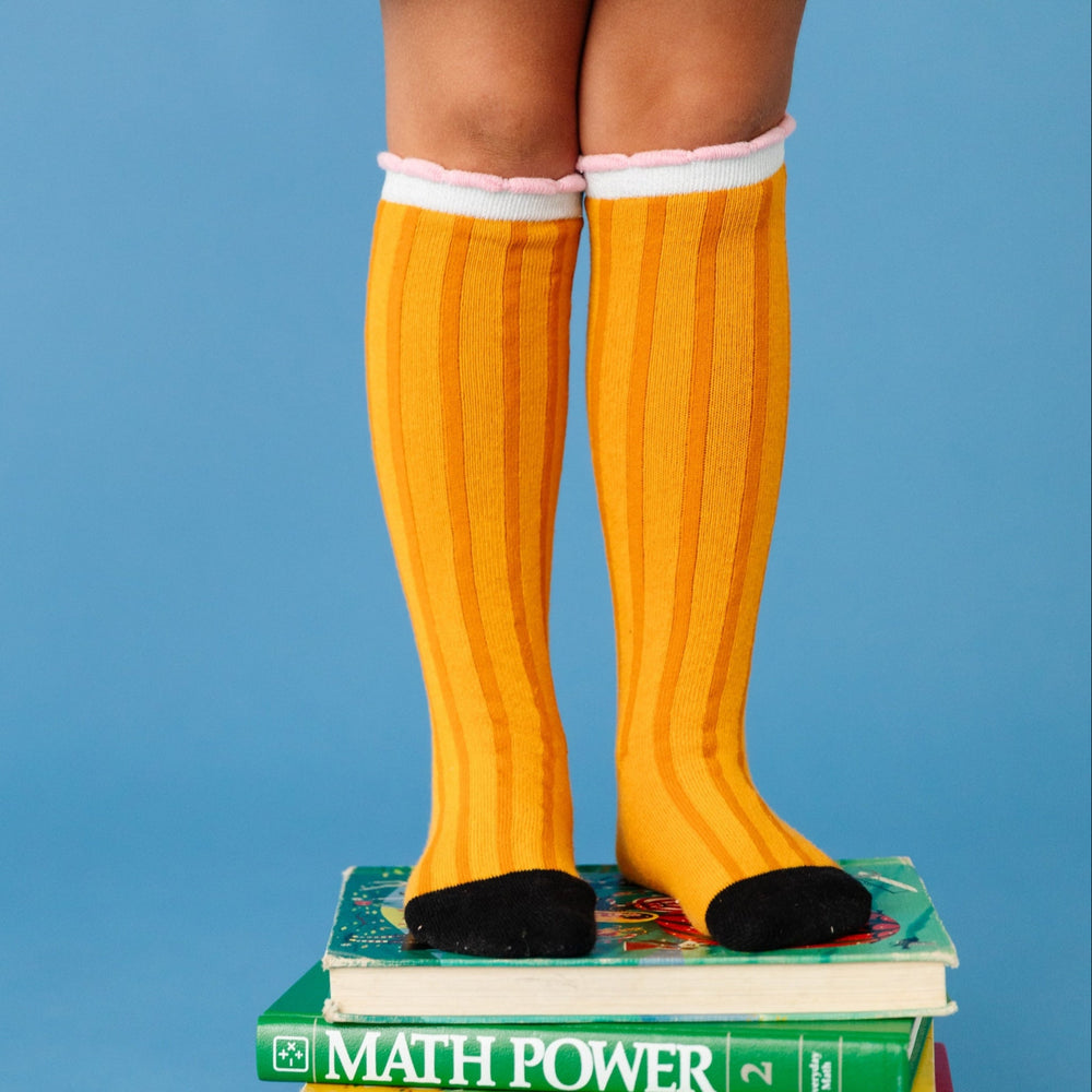girl wearing knee high socks with pencil design standing on books