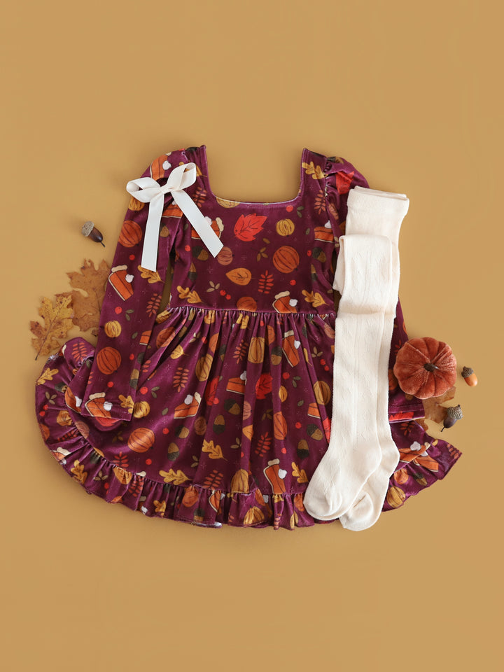 flat lay styled photo for plum velvet long sleeve twirl dress with pumpkin, pie and fall leaf print for Thanksgiving