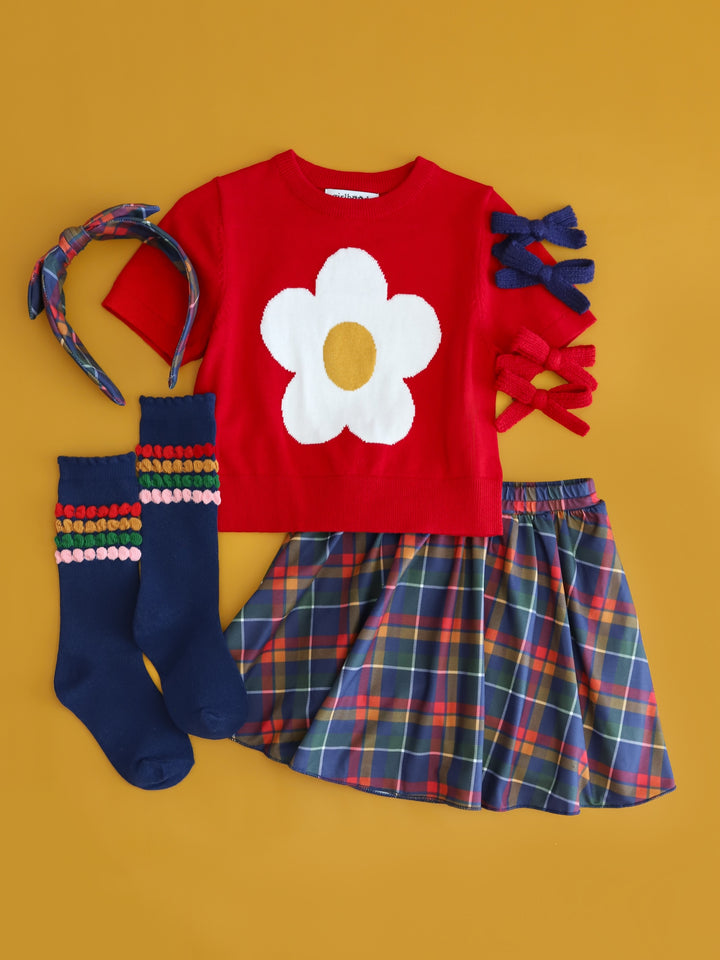 flatlay of girls back to school outfit with red short sleeve sweater with white flower, matching plaid skort, navy knee highs with school color bubble lines and matching bows and headband