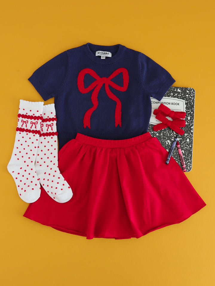 little girl's back to school outfit featuring navy short sleeve cotton knit sweater with red bow design and matching red skort with red bow knee highs and knit pigtail bows