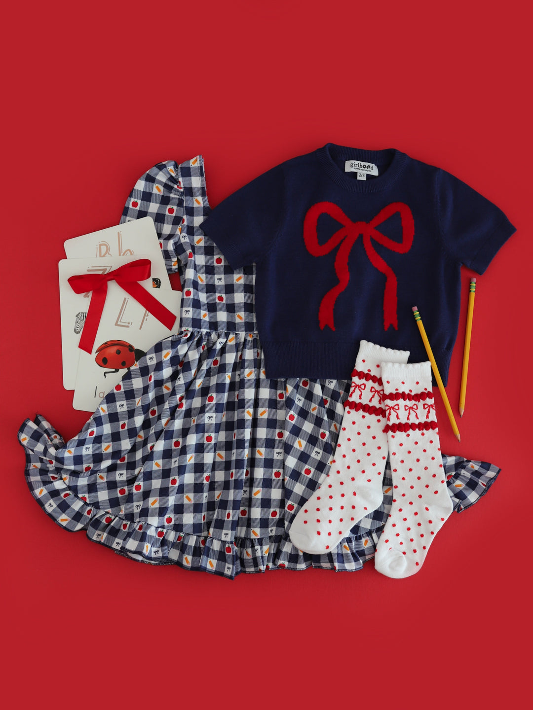 girl's back to school themed gingham twirl dress paired with navy short sleeve bow sweater and matching red bow knee highs