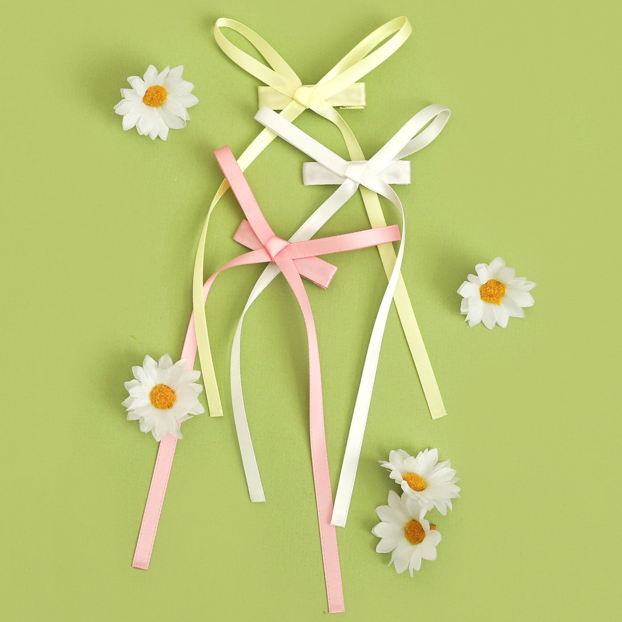 flatlay of girls' dainty long tail satin ribbon on clips in sunshine yellow, white, and blossom pink for spring