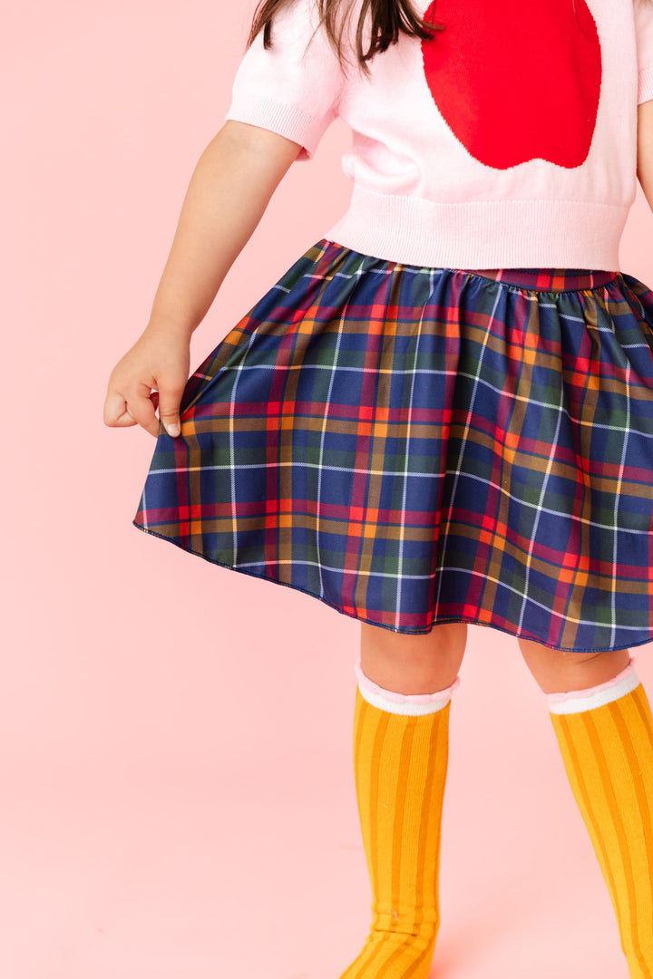 closeup of schoolgirl plaid skort paired with short sleeve apple sweater and knee highs with pencil design