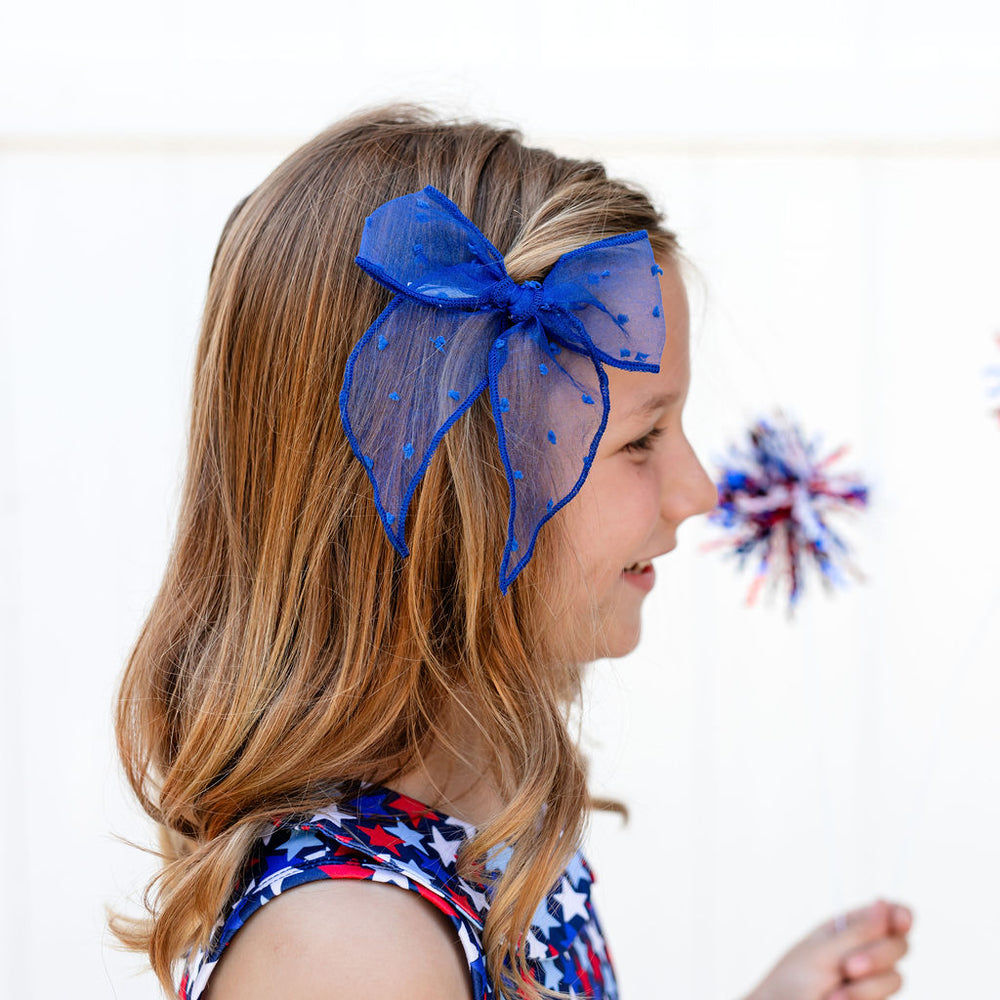 little girl in star print 4th of july dress with sheer blue fabric bow in her hair