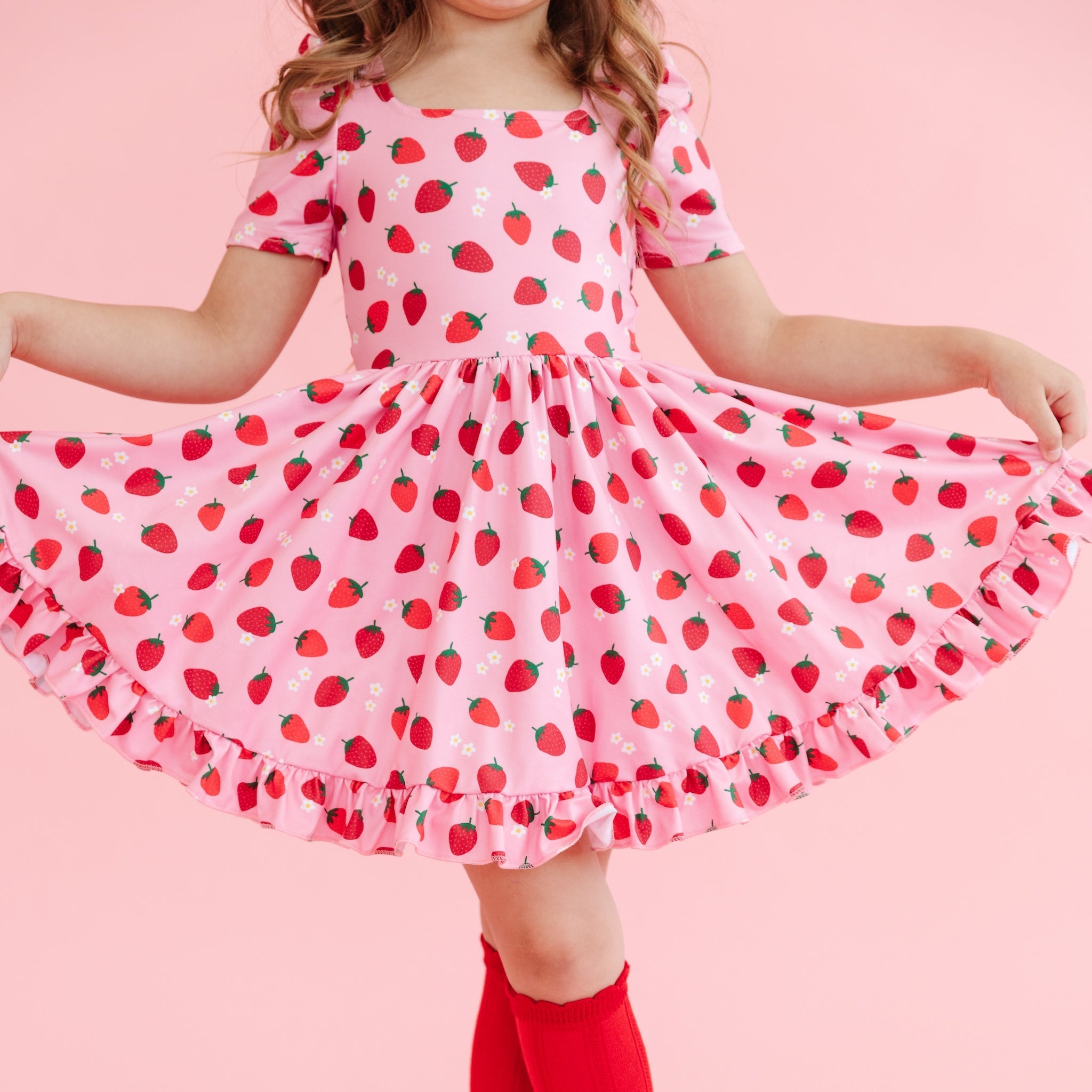 girl wearing girls' pink short sleeve twirl dress with red strawberry print and dainty white flowers and matching red knee high socks