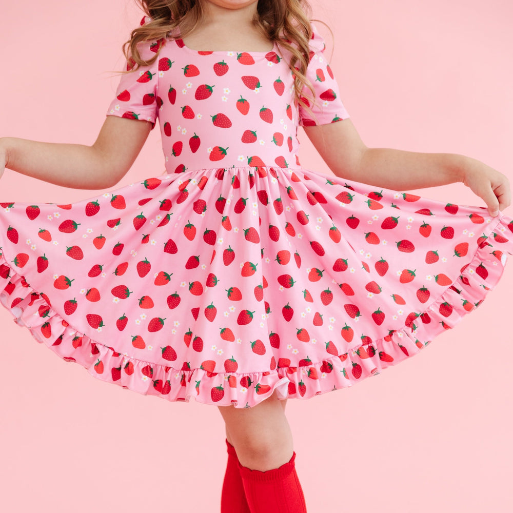 girl wearing girls' pink short sleeve twirl dress with red strawberry print and dainty white flowers and matching red knee high socks