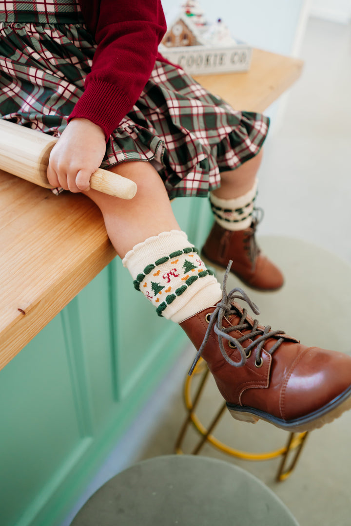 closeup of little girl baking in forest green plaid dress paired with cream knee highs with scalloped trim and fair isle print and little brown boots