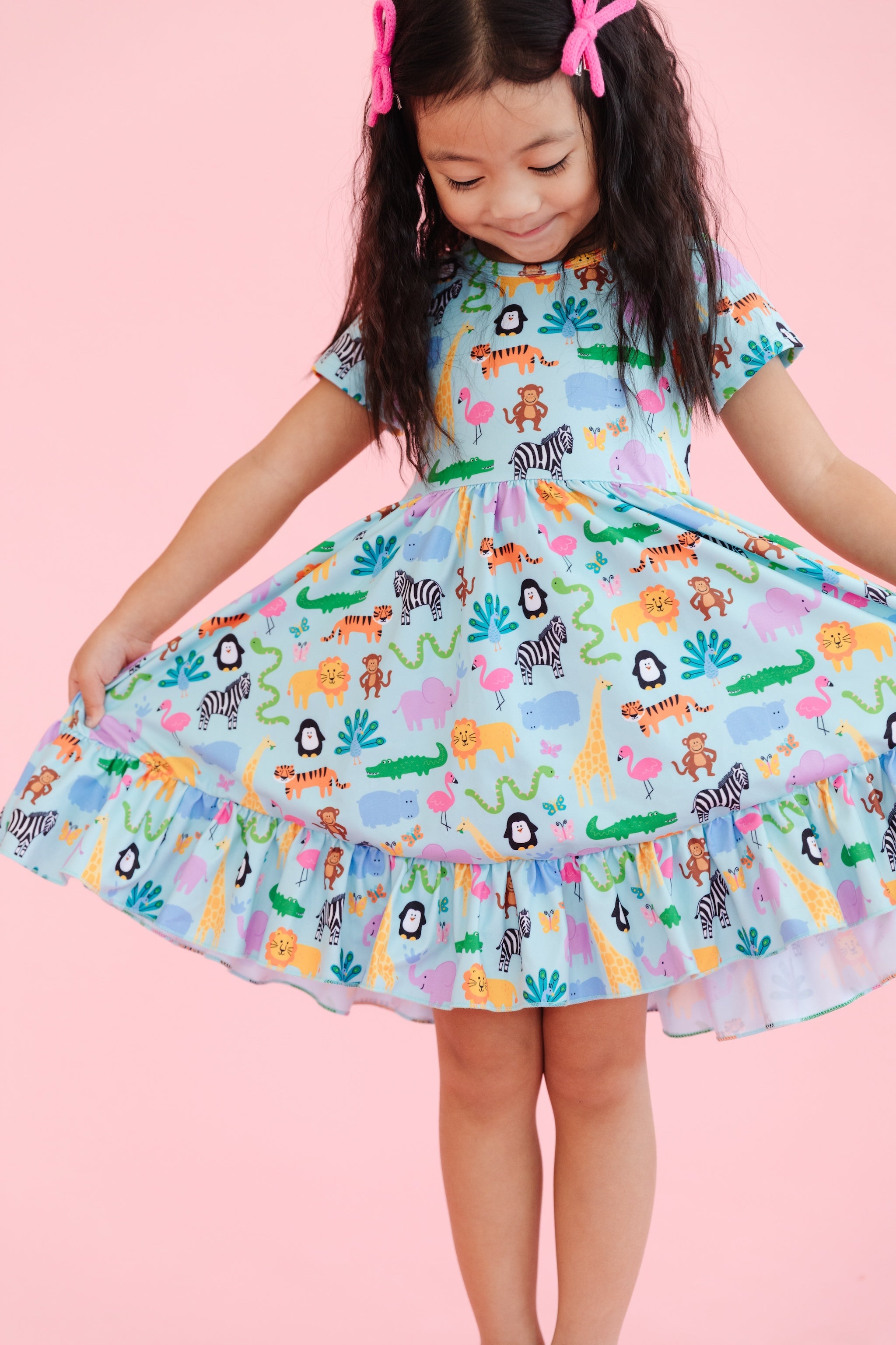 girl wearing short sleeve, ruffle hem twirl dress in mint with colorful zoo animal print and matching pink bows