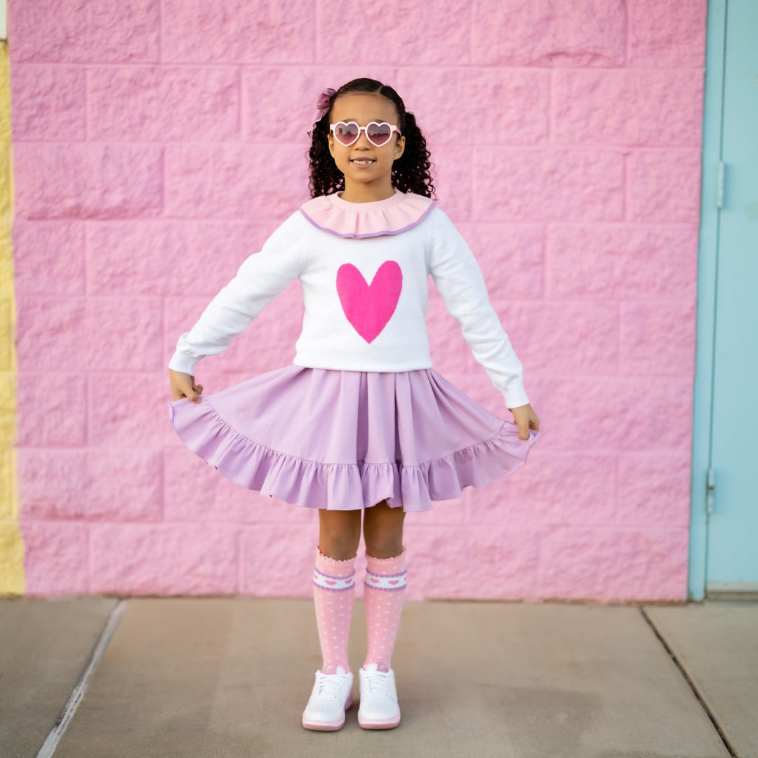 Girl in valentines outfit of purple dress white sweater with pink heart and pink knee high socks