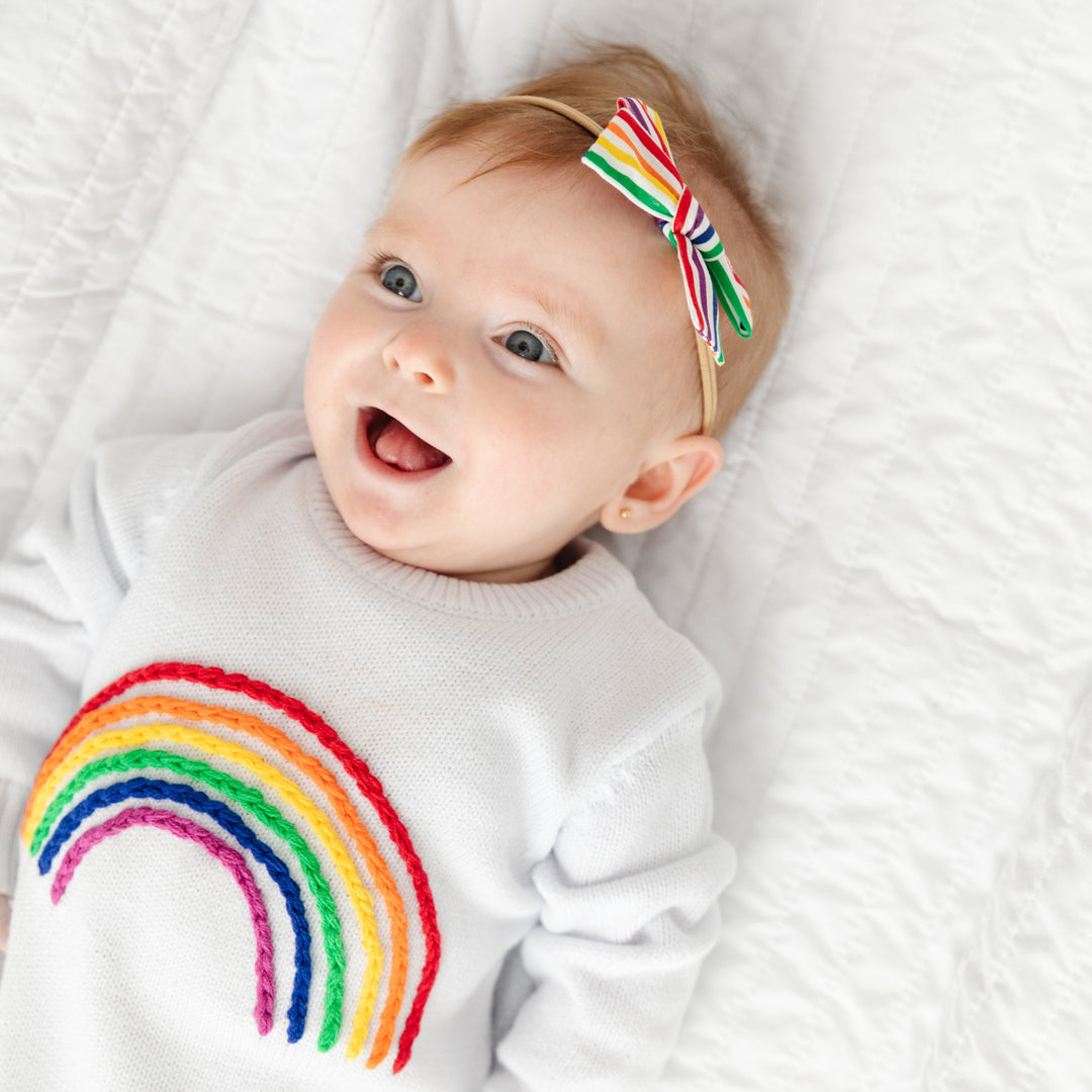 baby girl wearing rainbow embroidered sweater romper and rainbow stripe hair bow