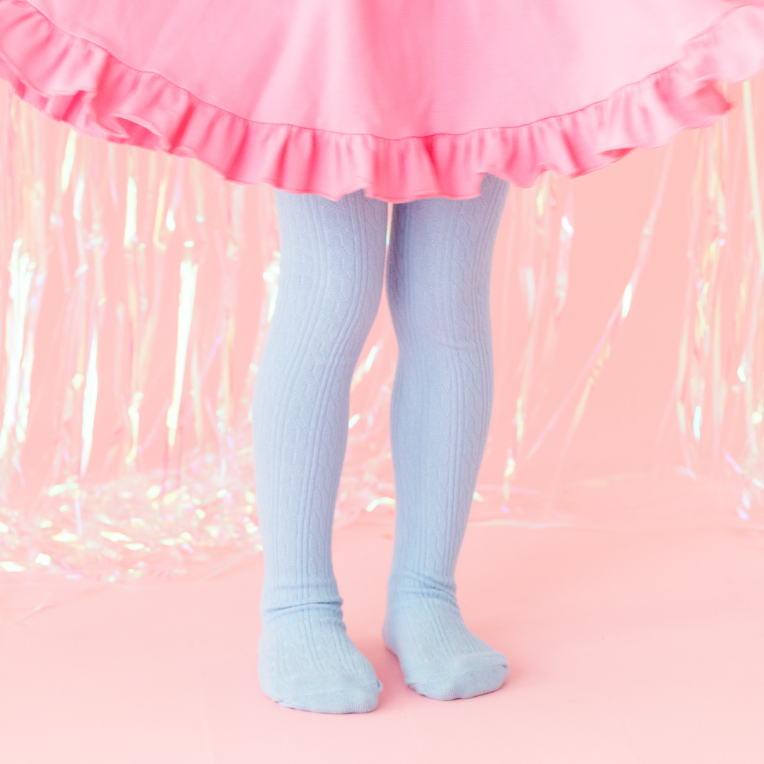 little girl sitting on wooden chair wearing white cable knit tights