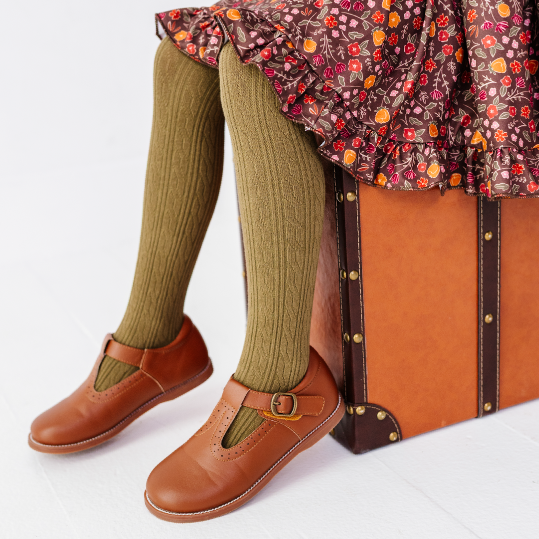 little girl sitting on wooden chair wearing white cable knit tights