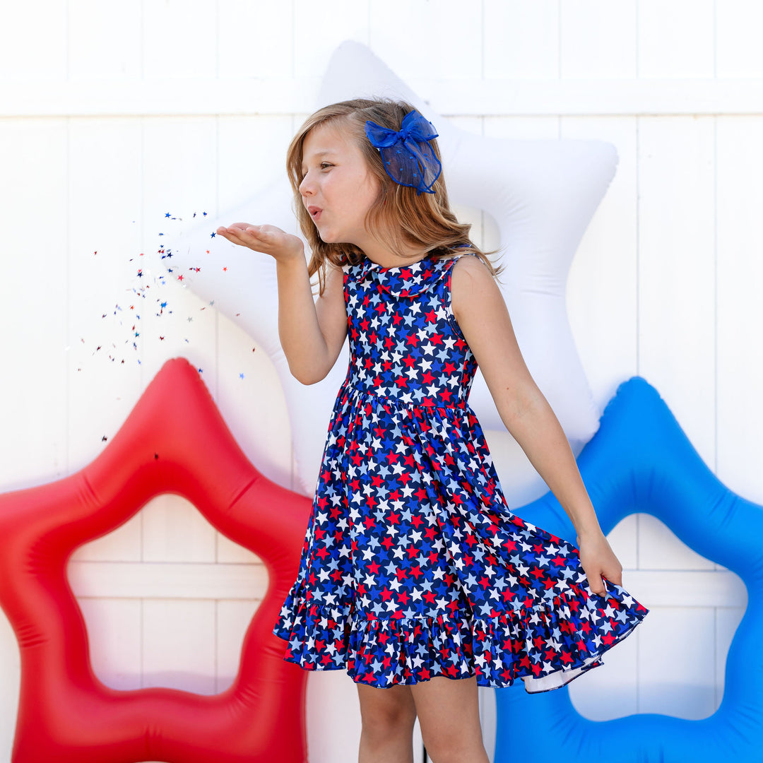 little girl blowing star confetti while wearing confetti inspired 4th of july star print dress