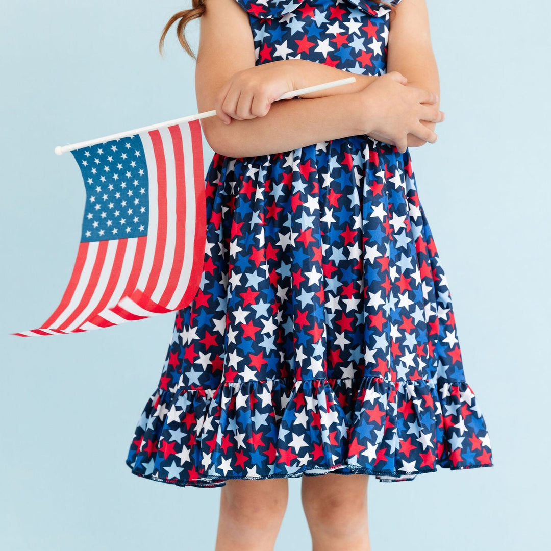 little girl wearing star print 4th of july print dress holding american flag
