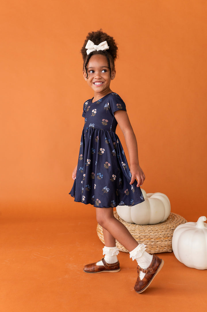 little girl posing in front of white pumpkins in navy blue floral v-neck twirl dress paired with cream lace top bobby socks and cream velvet hair bow