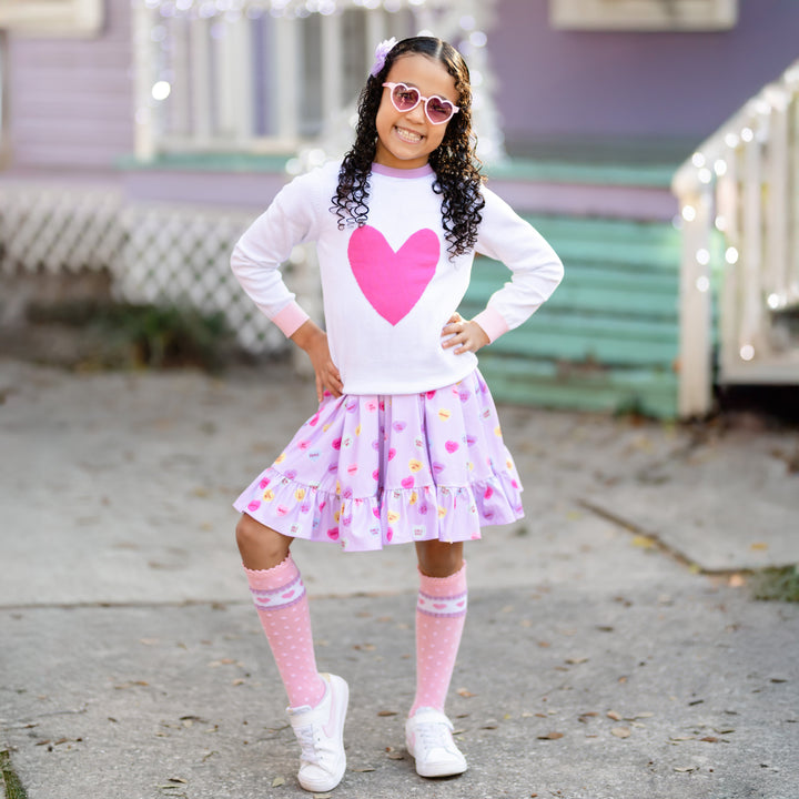 little girl in lavender heart dress, white knit sweater with pink heart and matching pink pattered Valentine's knee high socks