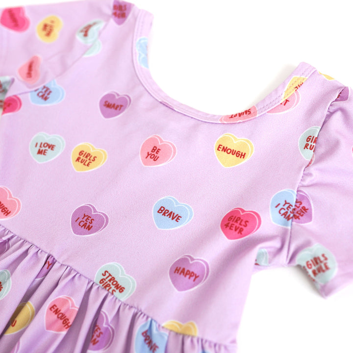 Closeup of multicolor conversation heart print on purple dress with words of affirmation for girlhood